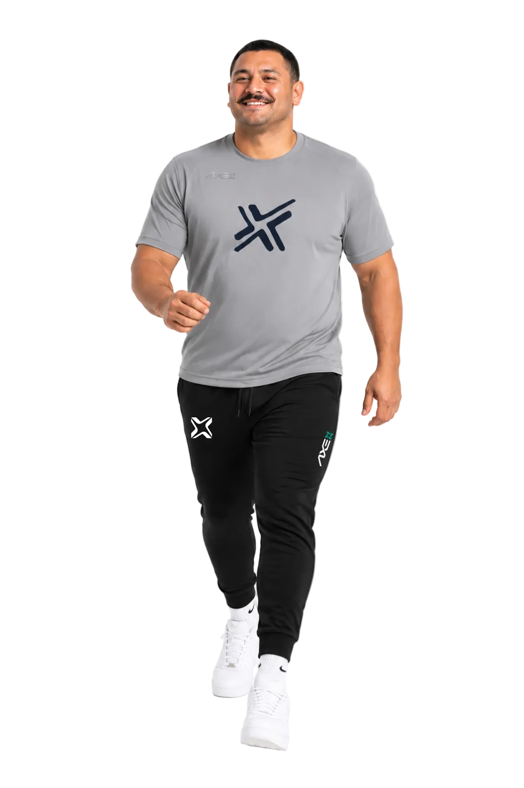 A man wearing a gray athletic t-shirt and black jogger pants with white sneakers, walking forward against a plain white background.