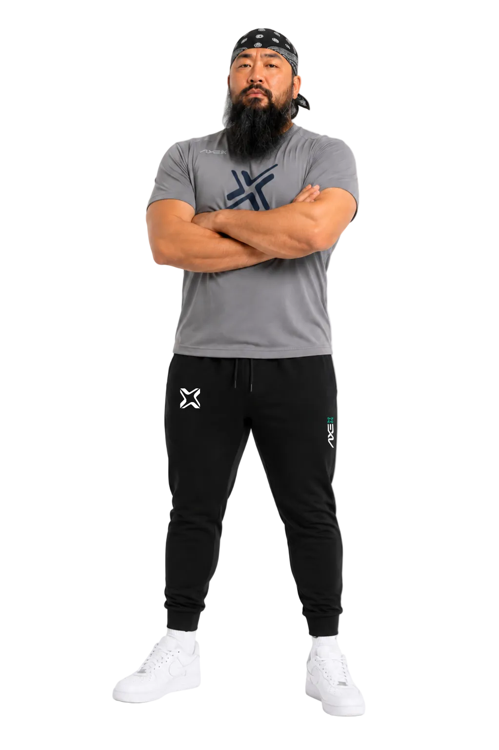 A man modeling a gray crewneck t-shirt and black jogger sweatpants with white sneakers, standing against a light gray background.
