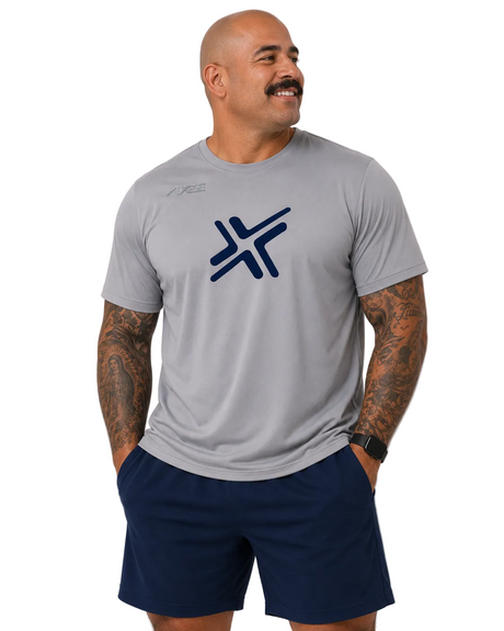 A man wearing a light gray athletic t-shirt with a dark blue geometric logo on the chest, paired with navy blue shorts, standing against a light gray studio background.