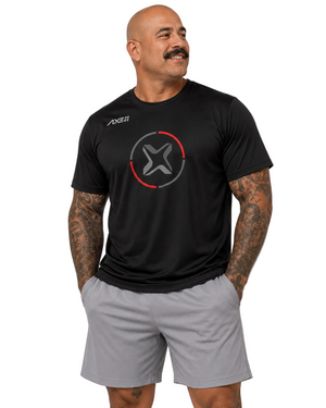 A man wearing a black athletic t-shirt with a red and gray circular logo on the chest and light gray athletic shorts, standing against a light gray studio background.