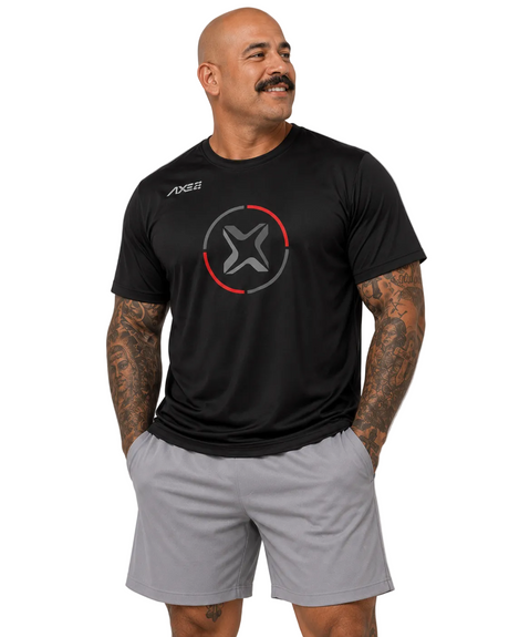 A man wearing a black athletic t-shirt with a red and gray circular logo on the chest and light gray athletic shorts, standing against a light gray studio background.