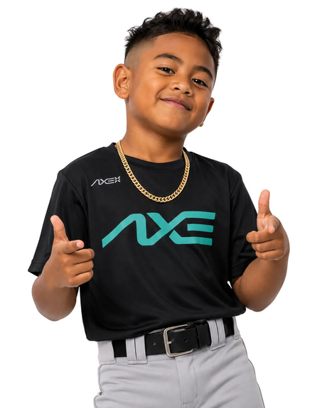 A young boy modeling a black short-sleeve t-shirt with a large teal 'AXE' logo on the front and a smaller white 'AXE' logo on the right chest, paired with gray baseball pants and a gold chain necklace, posing with thumbs up against a white background.
