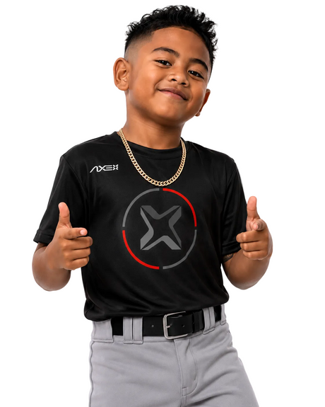 A young boy modeling a black short-sleeve athletic t-shirt with a gray and red circular logo on the chest and a white AXE brand logo on the right chest. He is also wearing a gold chain necklace, a black belt, and gray pants, posing with his thumbs up against a solid white background.