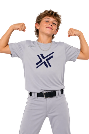 A young boy posing in a light gray short-sleeve athletic t-shirt with a navy blue logo on the chest, paired with matching gray baseball pants and a black belt, against a solid white background.