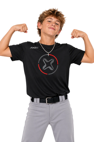 A young boy modeling a black short-sleeve t-shirt with a gray and red circular logo on the chest, paired with gray pants and a silver necklace, posing with flexed biceps against a light gray background.