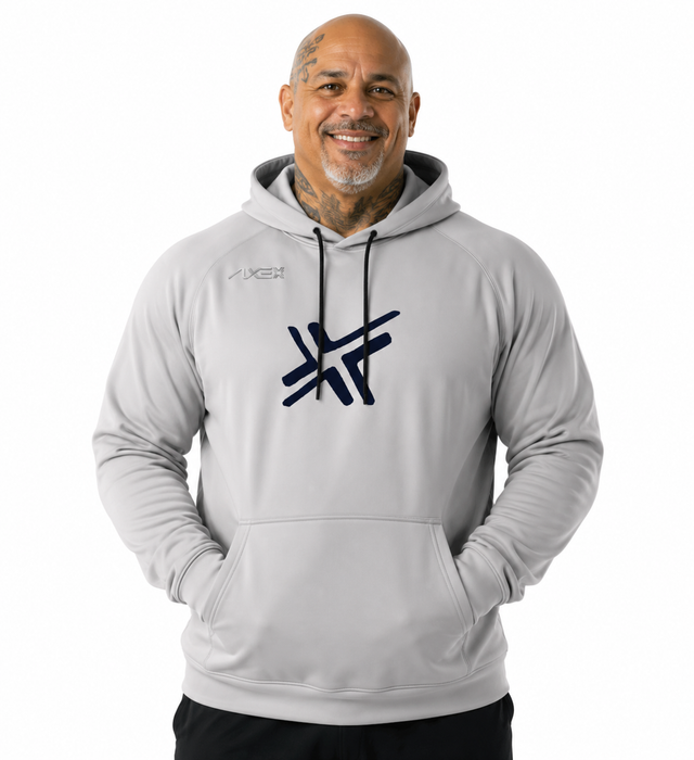 A smiling man wearing a light gray pullover hoodie with a dark navy graphic logo on the chest and a smaller logo on the left chest, photographed against a plain white background.
