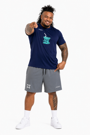 A man modeling a navy blue short-sleeve t-shirt with a teal graphic on the chest and gray athletic shorts, posed against a solid white background.