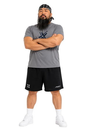 A man modeling a gray short-sleeve athletic t-shirt and black athletic shorts against a plain white background. The t-shirt features a dark blue geometric logo on the chest, and the black shorts feature white logos on the left leg.