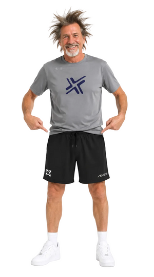 A man modeling a gray athletic t-shirt and black athletic shorts with white sneakers, pointing at the logos on the front of the shirt and shorts against a white background.